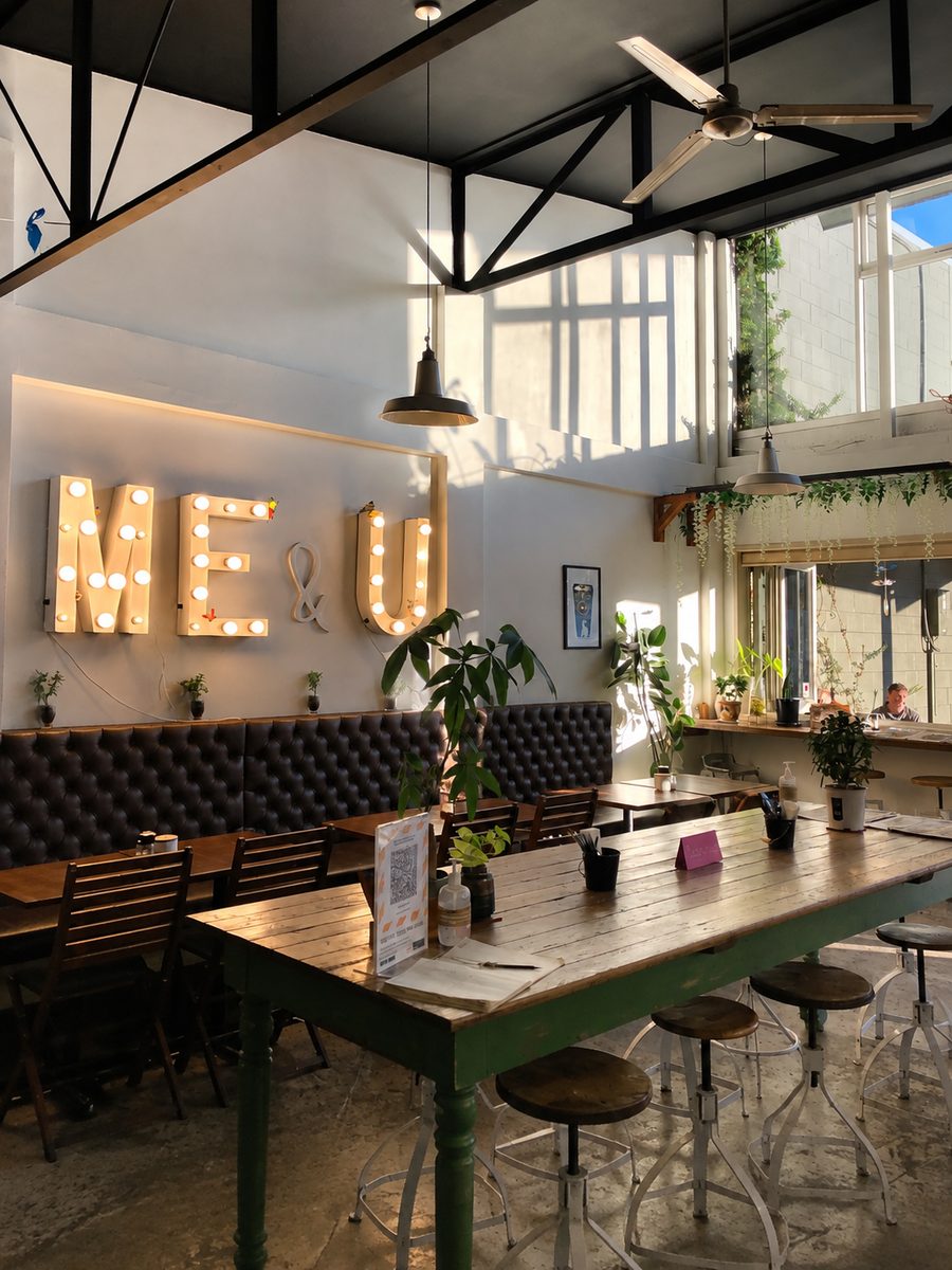 The sunlit interior of Me & You Cafe with communal tables and pendant lights